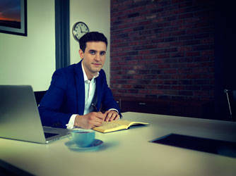 A man in a navy suit sitting at a desk with a book