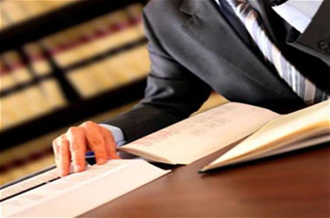 A man in a black suit sitting at a desk with a book