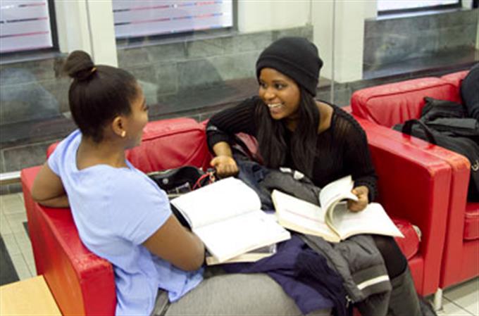 Two Women smiling while sitting on a red couch sharing their books