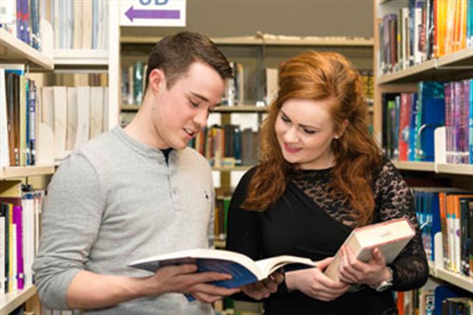 Two students studying a book in the DBS library
